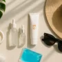 Flat lay of SPF 50+ sunscreen, hydrating serums, cooling gel pack, hat and sunglasses with tropical leaf—post-treatment pigmentation care in Singapore.