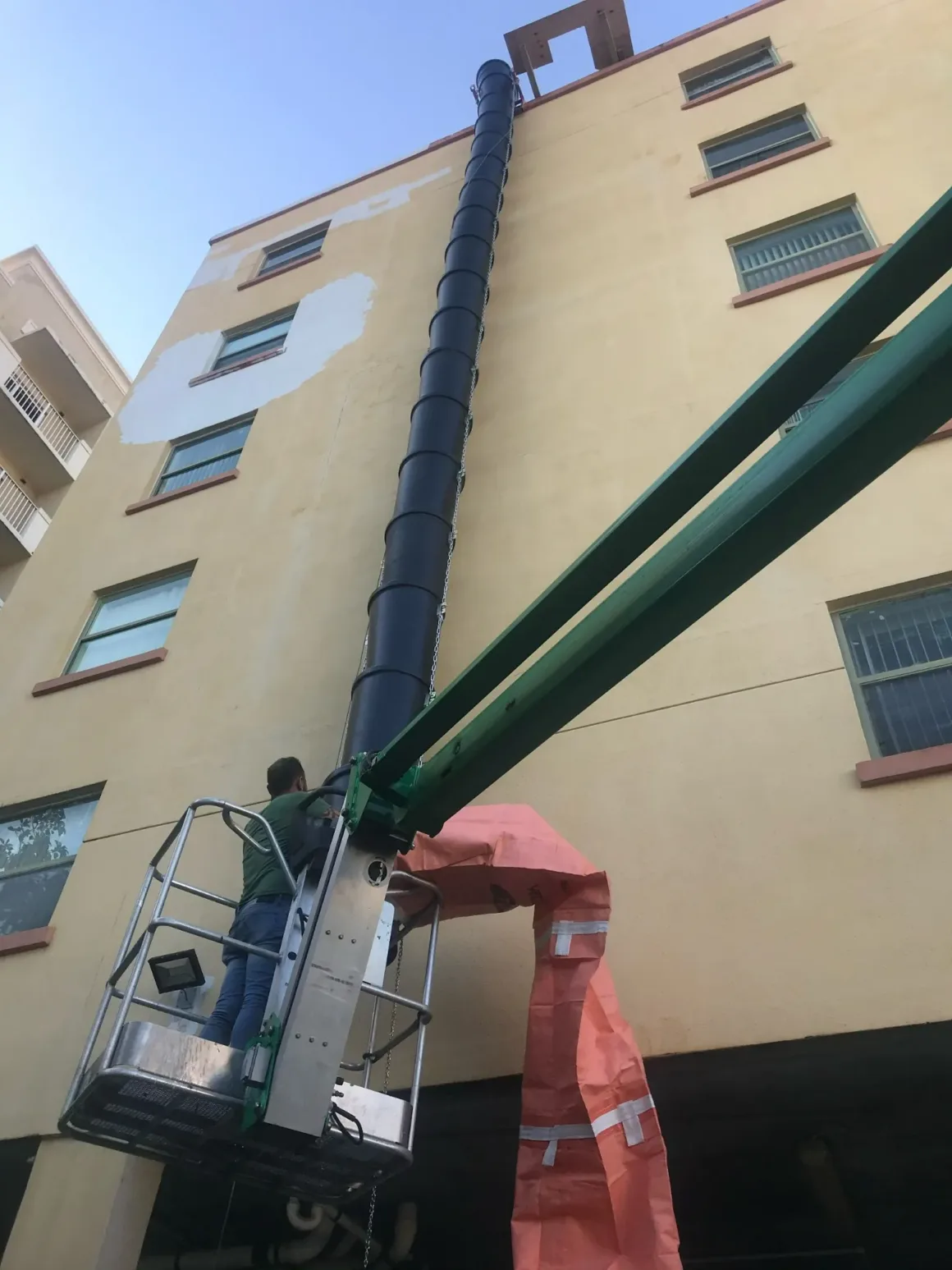 plastic debris chutes installed on a mid-rise building, feeding demolition waste to a container