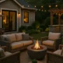 Twilight backyard outdoor living space with a fire pit, cushioned seating, dining table, and an outdoor kitchen under a wooden pergola.