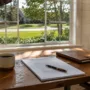 A sunlit home office desk with real estate contract documents and a view of a suburban lawn