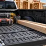 A clean pickup truck bed coated with a textured black spray-in bed liner filled with contractor tools and lumber