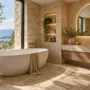A luxury European-inspired bathroom featuring warm travertine stone walls, a freestanding soaking tub, an arched mirror, and brushed brass tapware.