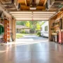 An organized residential garage featuring wall-mounted slatwall racks, clear plastic storage totes on industrial shelves, and overhead ceiling racks