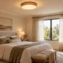 A modern bedroom illuminated by a warm LED flush-mount ceiling fixture and natural daylight